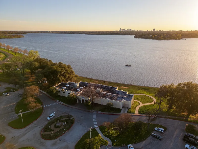 The Bath House Cultural Center on the White Rock Lake shore at sunset, with the Dallas skyline beyond