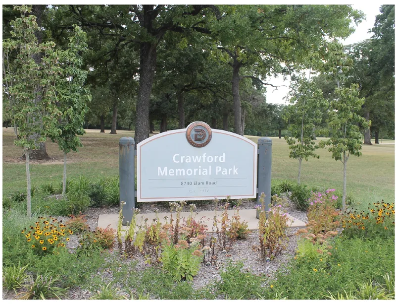 The Crawford Memorial Park entrance sign among wildflowers beneath the park’s old oaks