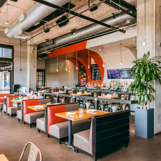The industrial-chic dining room at HG Sply Co. with orange booths and exposed concrete