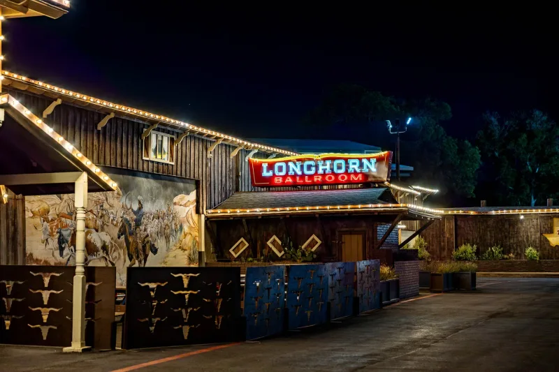 The Longhorn Ballroom’s neon sign and cattle-drive mural lit up at night