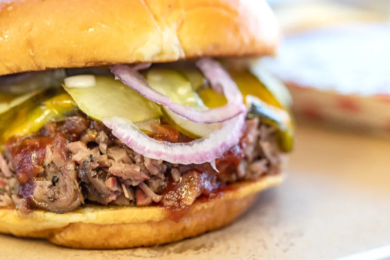 A smoked brisket sandwich stacked with pickles and red onion at One90 Smoked Meats
