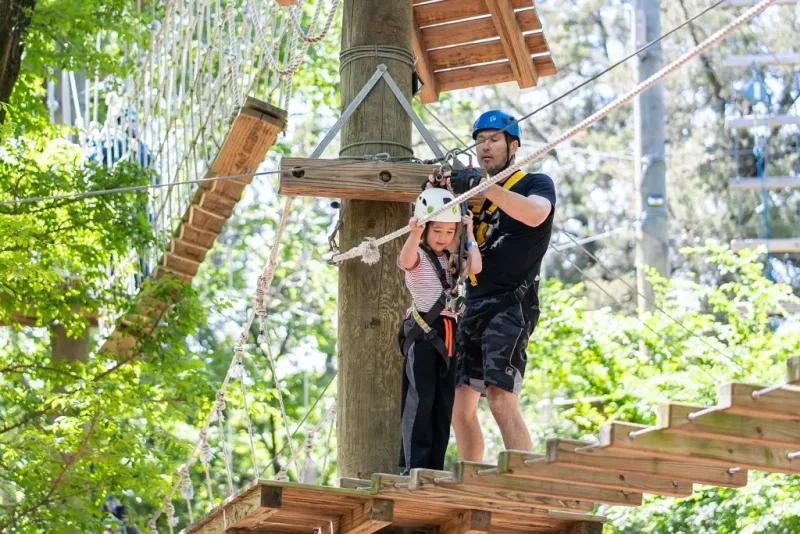 A parent and child crossing a treetop ropes course at Trinity Forest Adventure Park