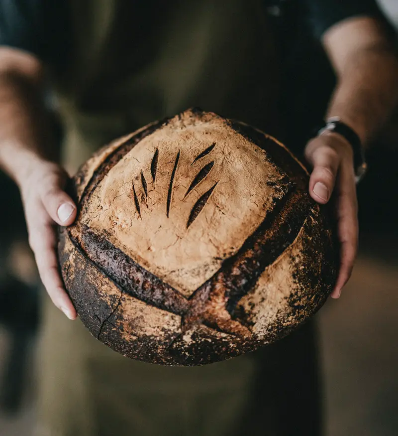 A Village Baking Co. baker holding a fresh sourdough boule