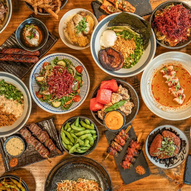 An overhead spread of Wabi House dishes — a ramen bowl, salads, edamame, karaage, and grilled skewers on a wood table