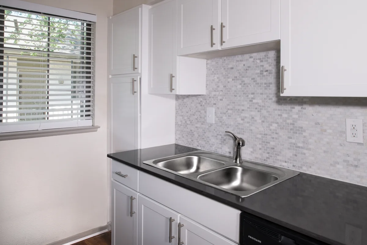 Galley kitchen with dark wood cabinets and double sink opening to a chandelier-lit hallway