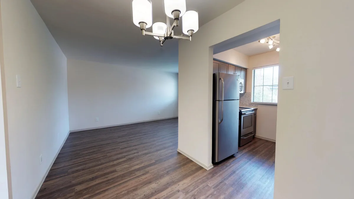 Dining area with chandelier and wood-look flooring opening to a stainless-appliance kitchen