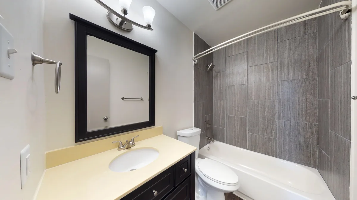 Bathroom with black-framed mirror, cream vanity and gray-tiled tub-and-shower surround