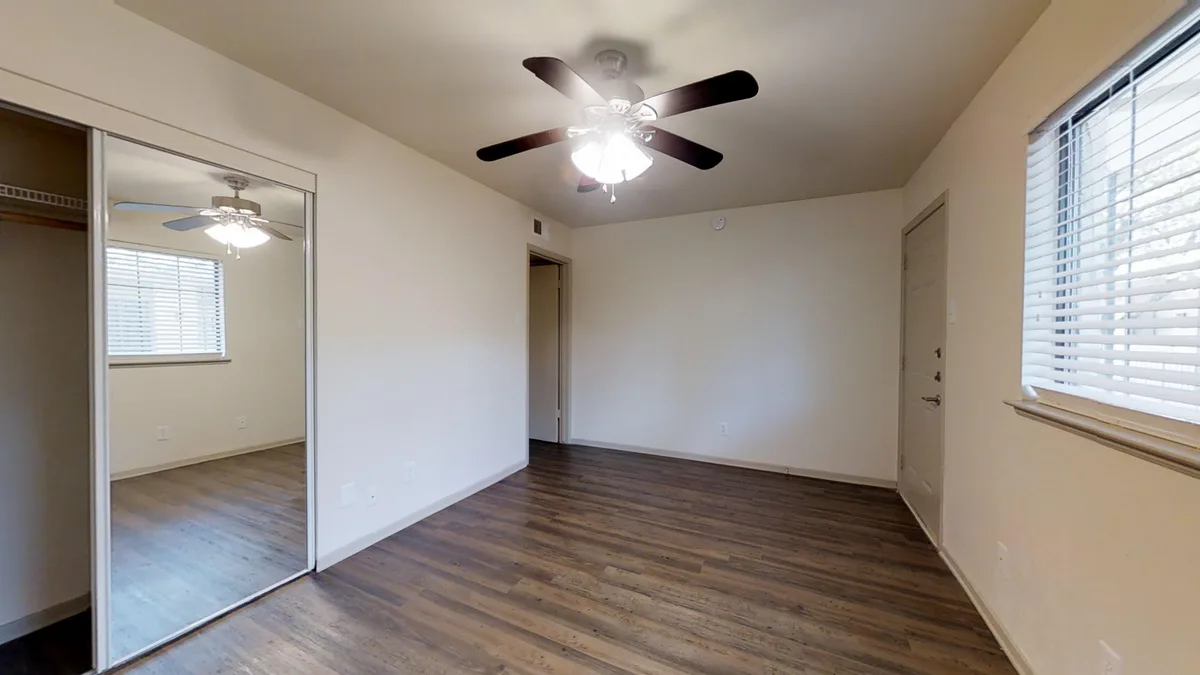 Bedroom with mirrored closet doors, ceiling fan and large window in wood-look flooring