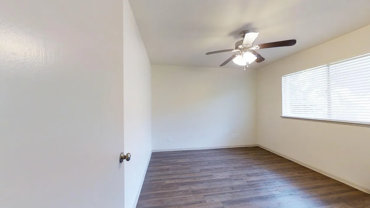 Bright bedroom with ceiling fan and oversized window over wood-look flooring
