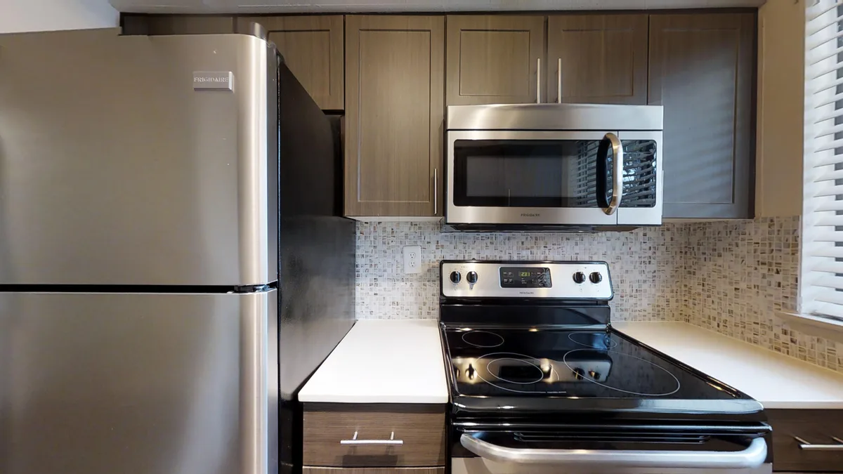 Stainless refrigerator, range and microwave set against a cream mosaic tile backsplash