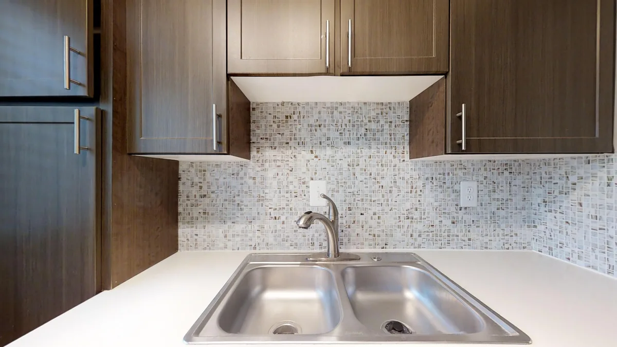 Stainless double-basin sink beneath espresso cabinets with cream mosaic tile backsplash