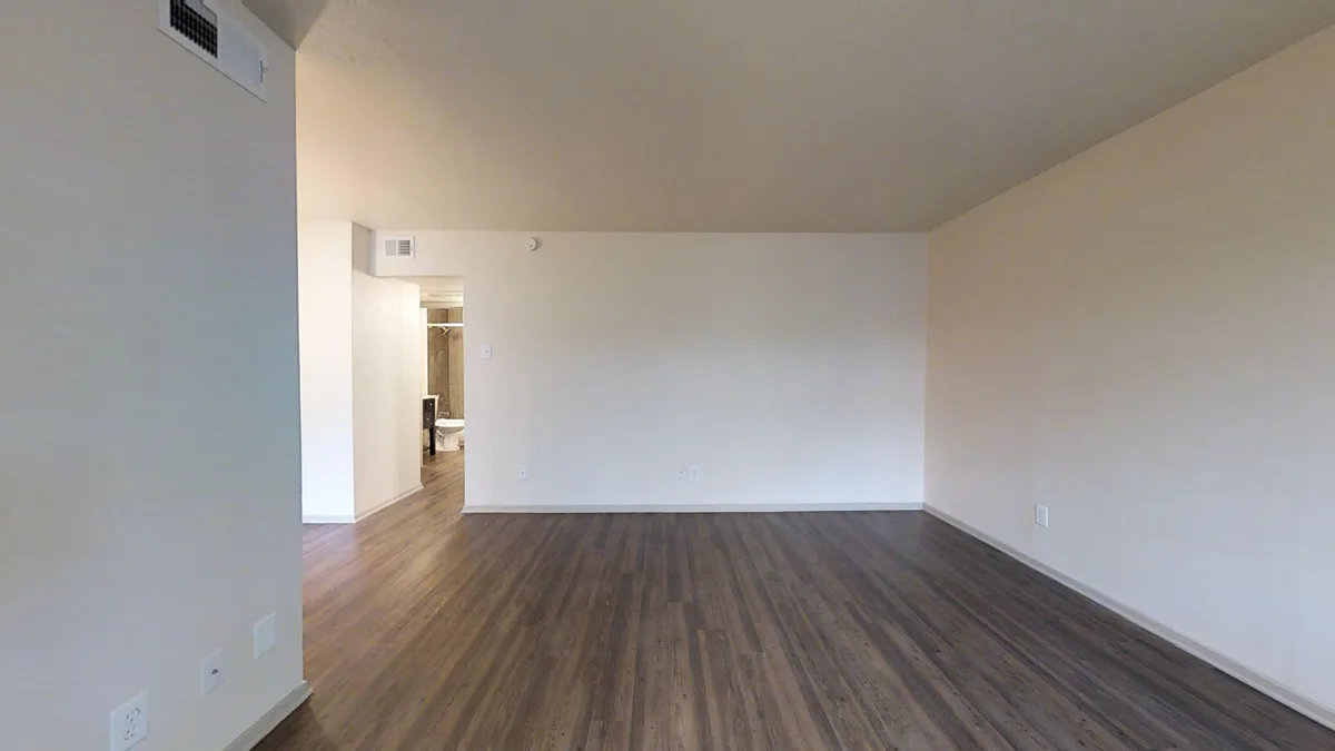 Large open living room with wood-look flooring and hallway toward the bathroom