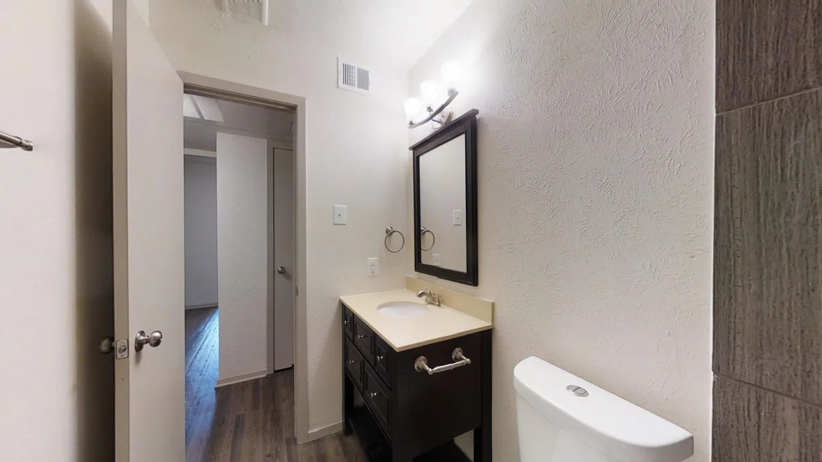 Bathroom with espresso vanity, framed mirror and gray-tiled shower beside the hallway
