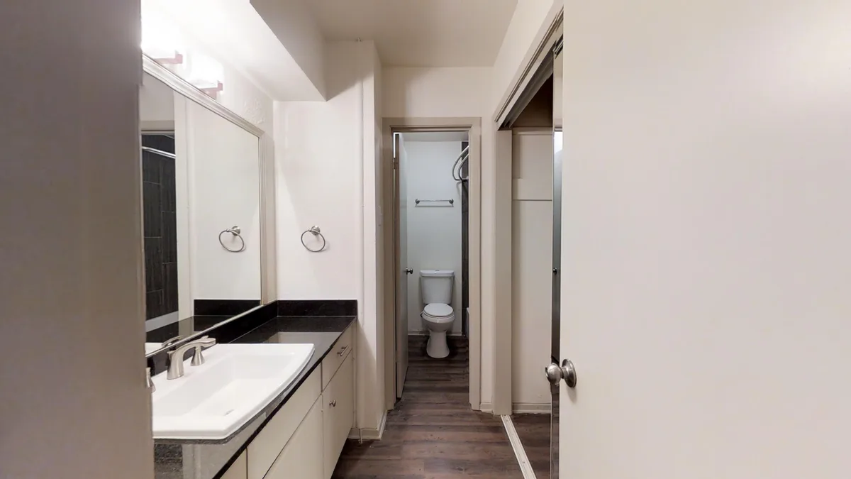 Dual-access bathroom with a dark vanity top, large mirror and separate toilet compartment