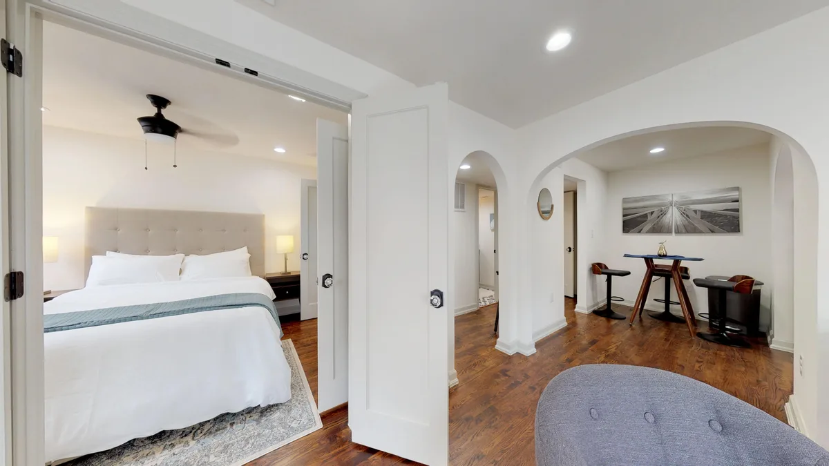 Bedroom with upholstered tufted headboard and black ceiling fan, seen through open double doors