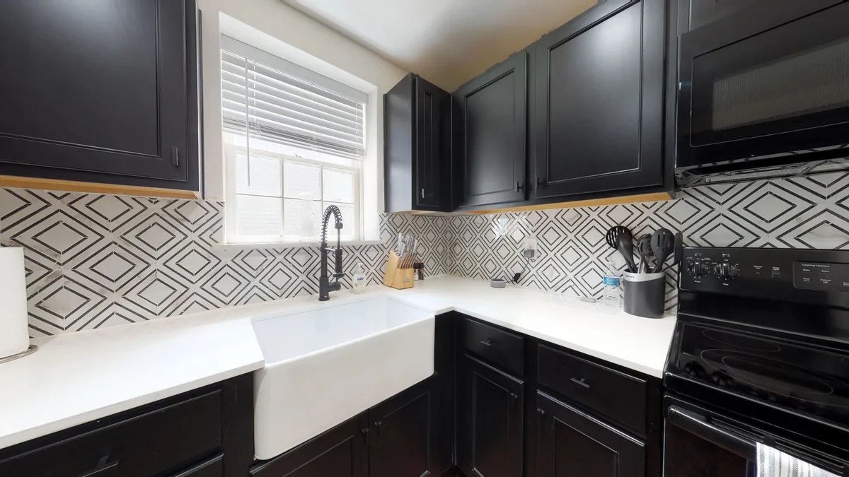 Kitchen corner with apron-front sink, black gooseneck faucet and black appliances beneath a bright window