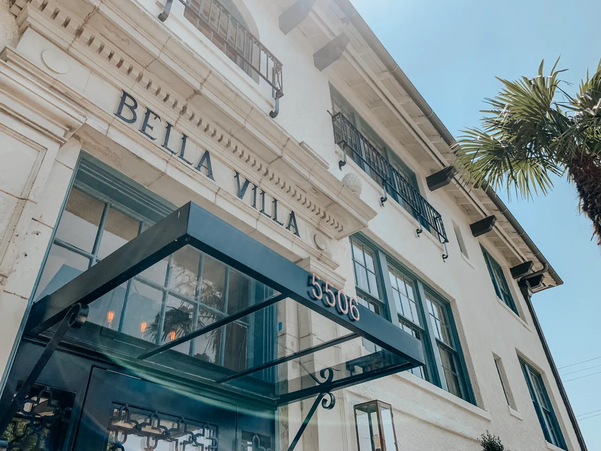 Low-angle view of the carved BELLA VILLA entrance and black canopy marked 5506 against a clear blue sky