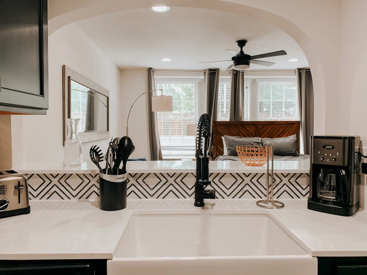 Farmhouse sink and black diamond-tile backsplash at the kitchen pass-through, bed visible behind