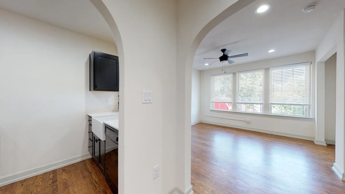 Unfurnished studio living space with hardwood floors, black ceiling fan and large blinds-covered windows