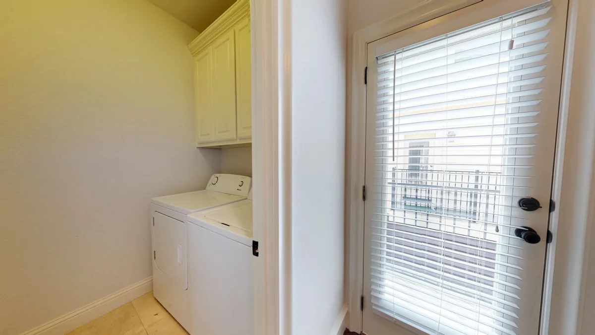 Laundry room with a top-load washer and dryer beside a blinded balcony door