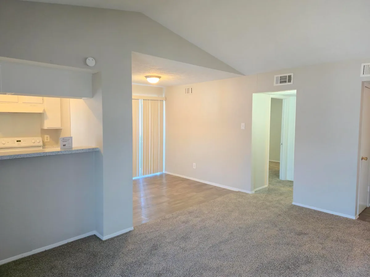Open living and dining room with a vaulted ceiling, wood-style plank flooring, and a breakfast bar off the kitchen