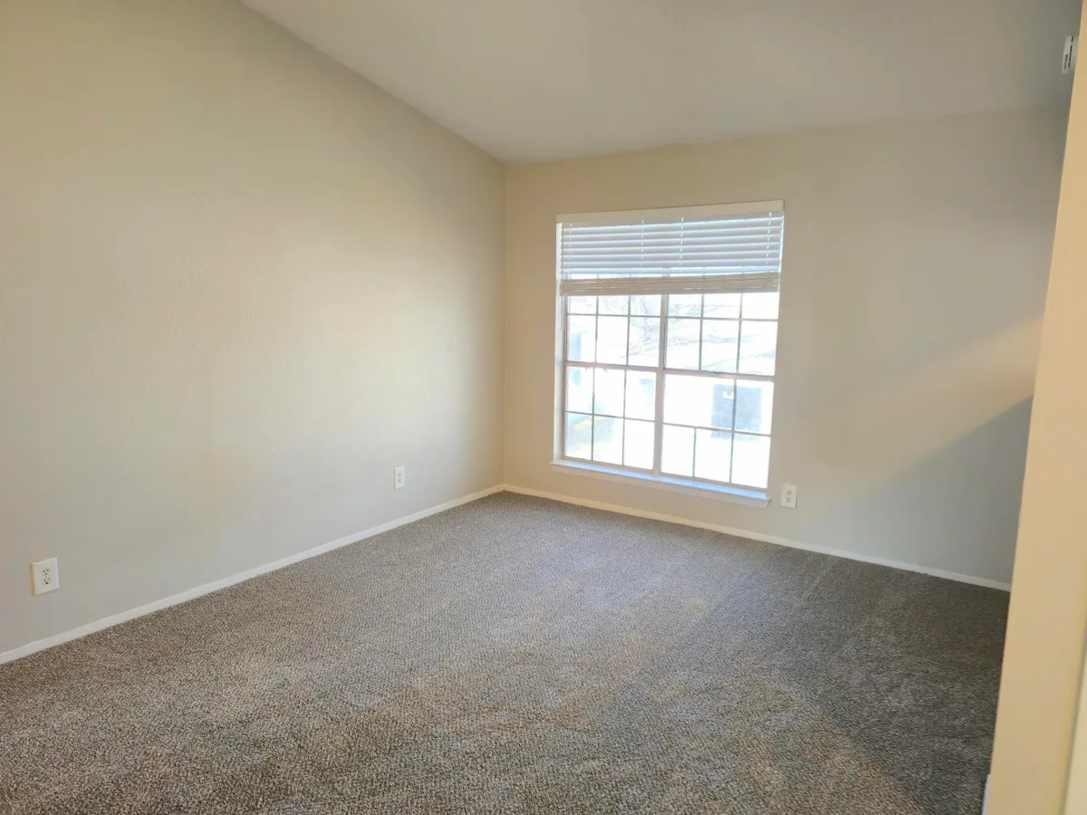 Carpeted living area with a large grid-pane window overlooking the community grounds