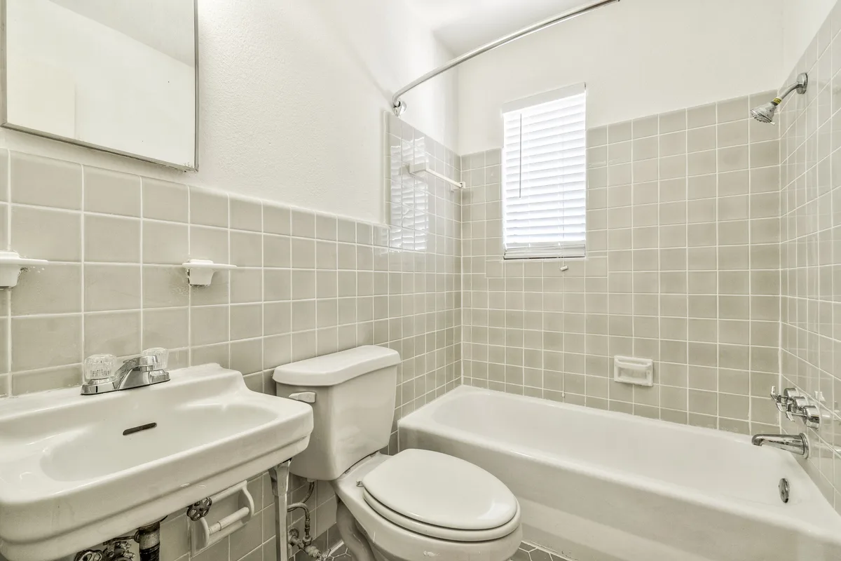 Bathroom with soft-gray wall tile, tub-shower, pedestal sink and blinded frosted window