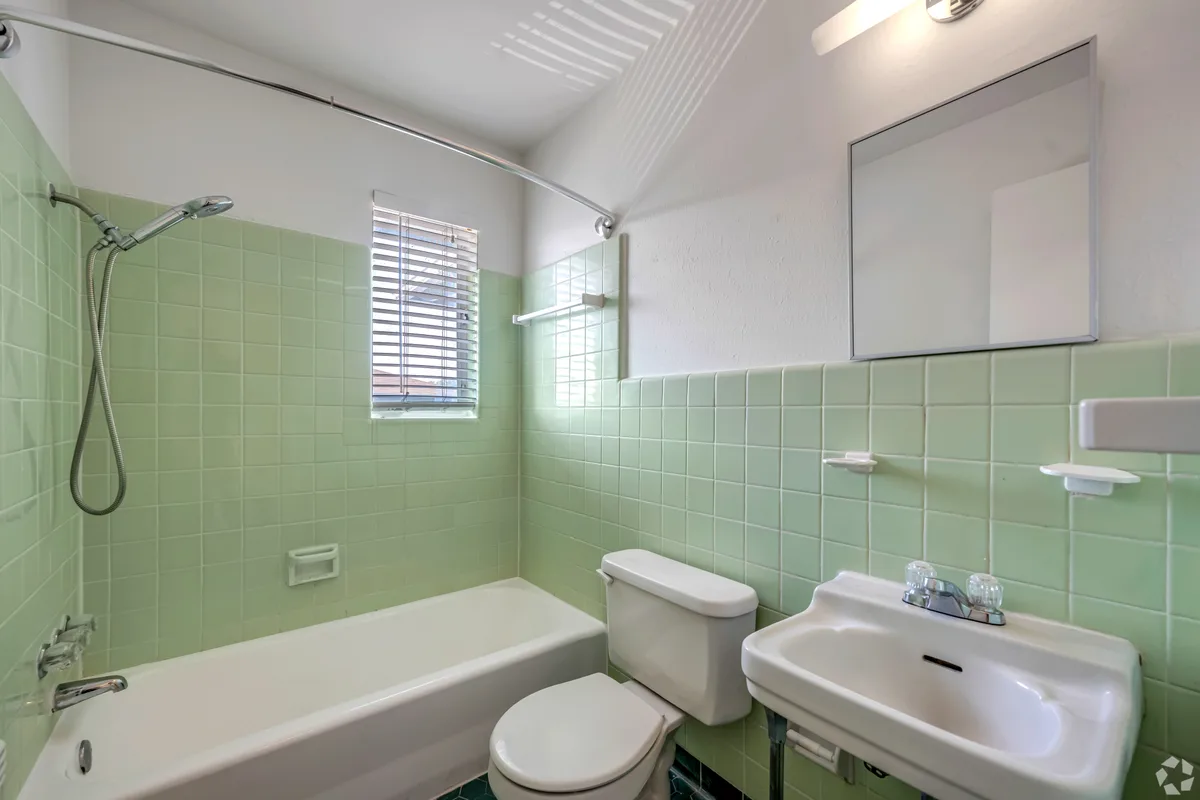 Retro bathroom with mint-green tile surround, tub-shower and framed mirror above the sink