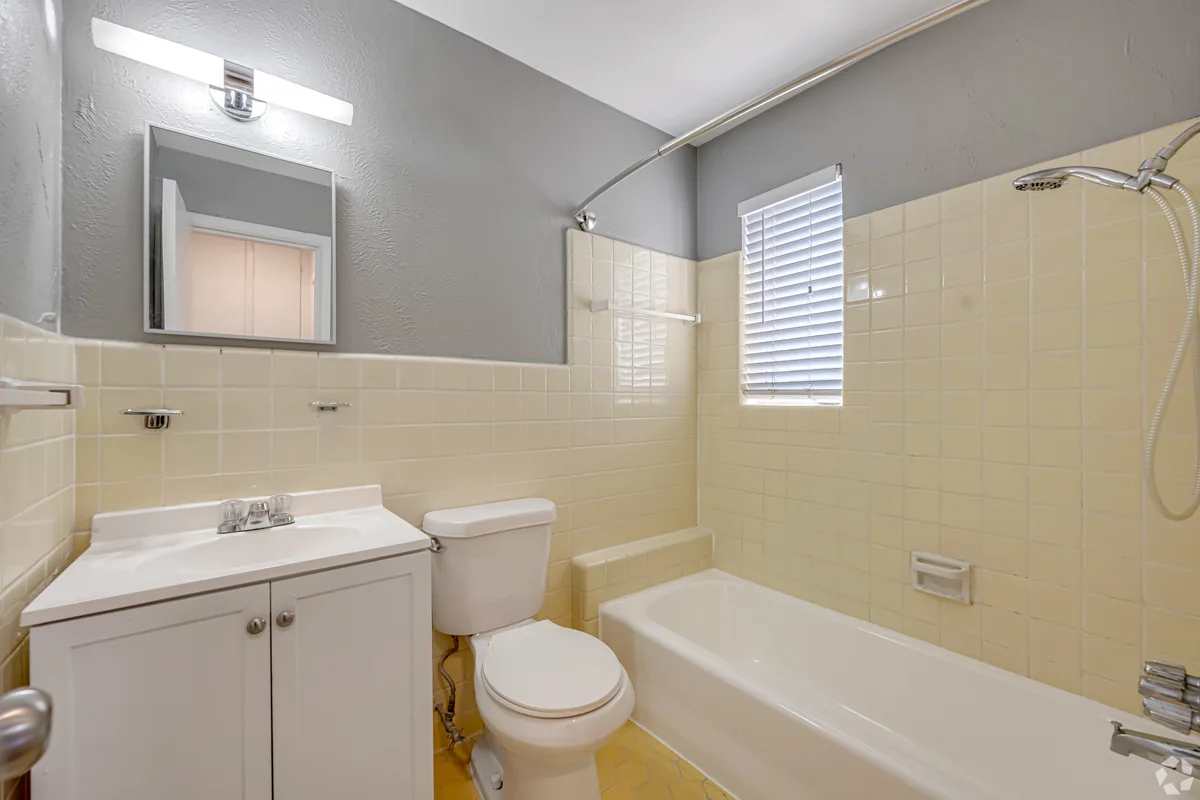 Bathroom with butter-yellow tile wainscot, gray walls, tub-shower and white vanity