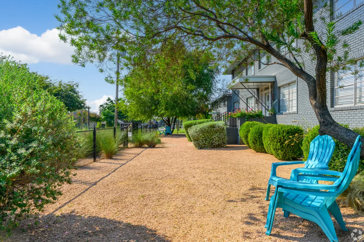 Gravel courtyard with turquoise Adirondack chairs and trimmed hedges along a shaded tree-lined path