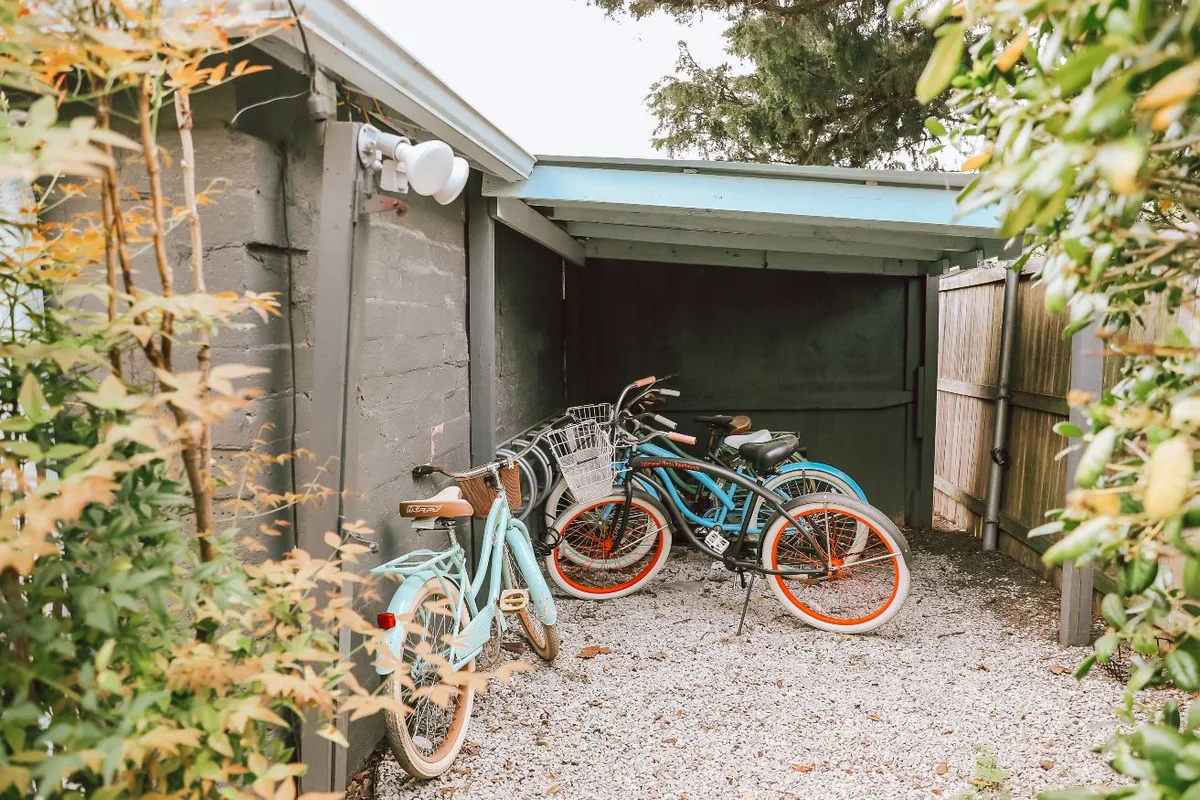 Complimentary cruiser bikes parked under a covered storage nook framed by leafy shrubs