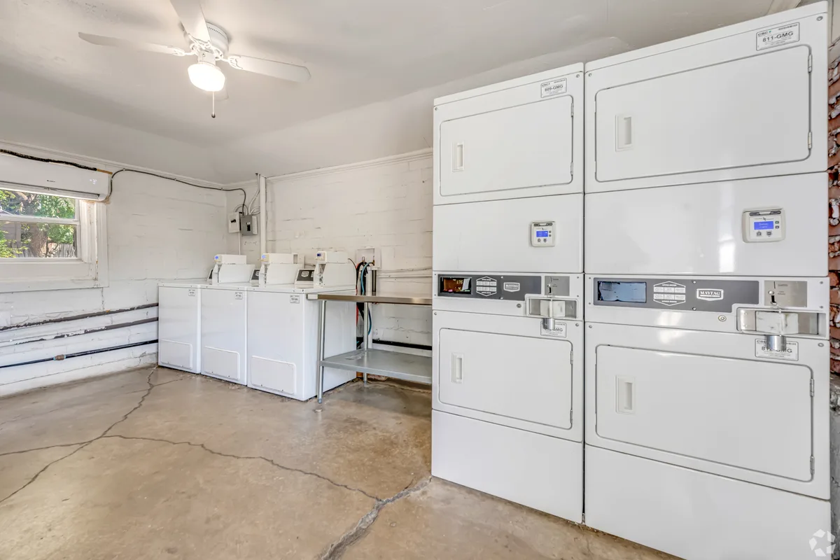 Shared laundry room with multiple stacked and front-load washers and dryers and a folding table