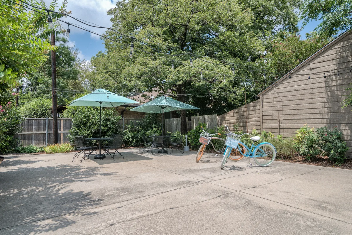 Patio lounge with green umbrellas, bistro seating and cruiser bikes shaded by mature oaks