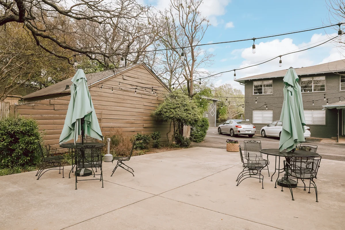 Shared concrete patio with wrought-iron bistro tables and umbrellas beneath residential buildings