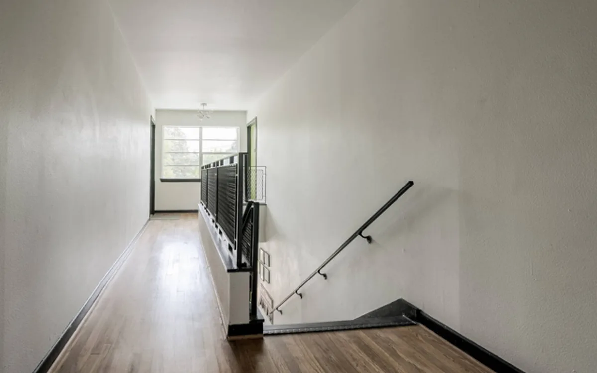 Bright interior stairwell landing with hardwood floors, metal railing and a large window