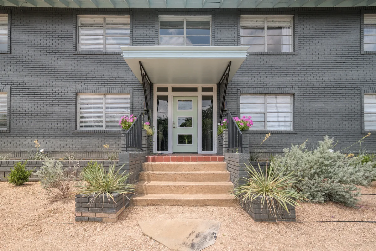 Mint-green front door beneath a cantilevered canopy framed by potted agave and blooming planters