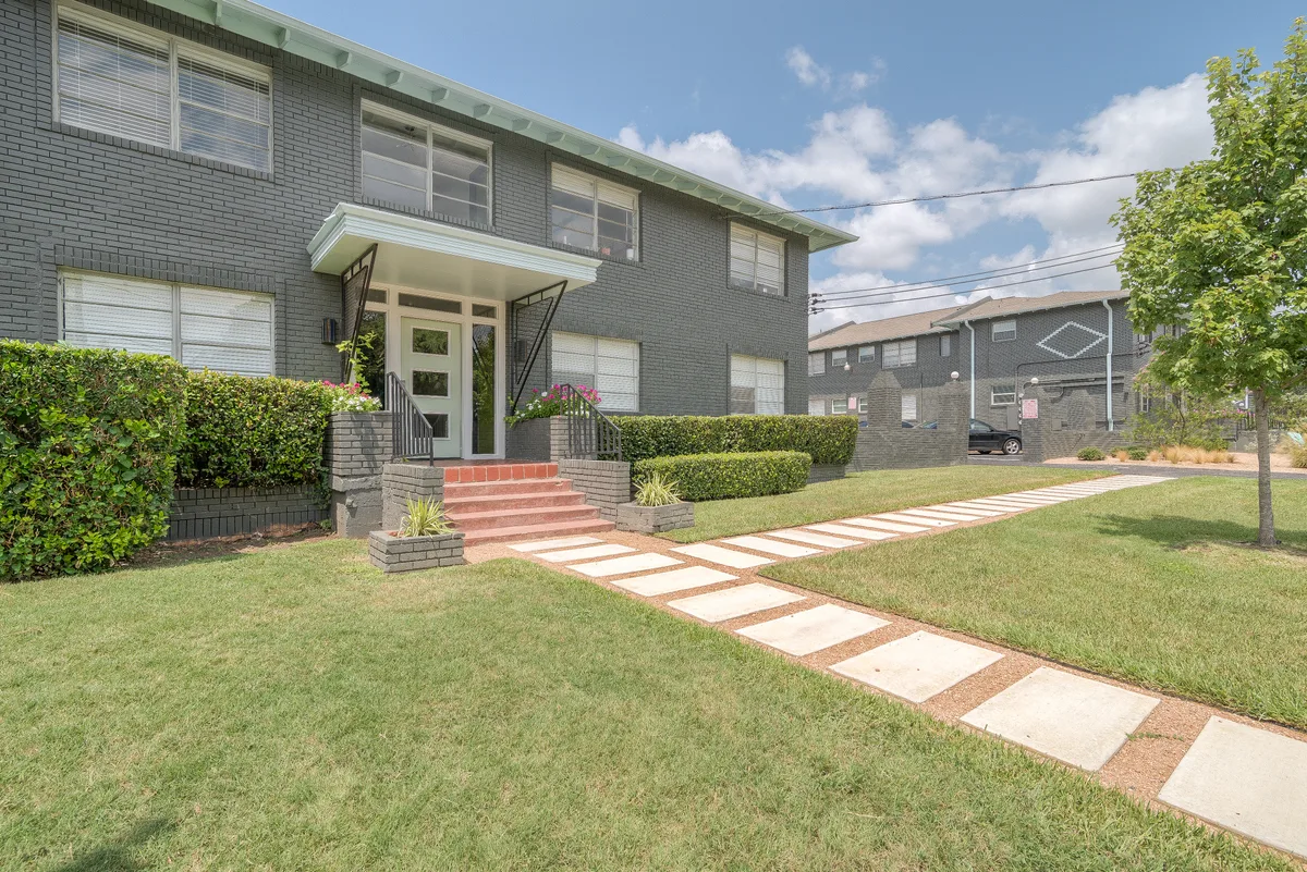 Manicured lawn and stepping-stone walkway leading to the gray brick building's covered entrance