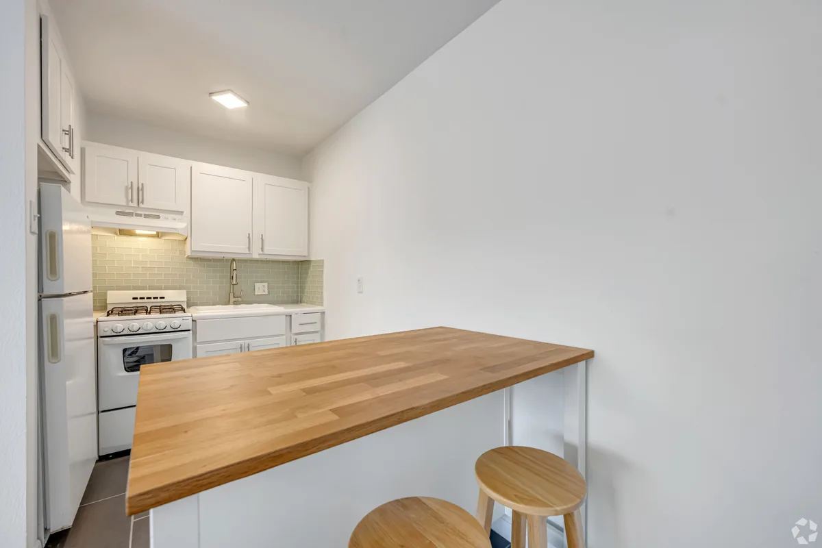 Compact white kitchen with gas range and butcher-block breakfast bar and wood stools