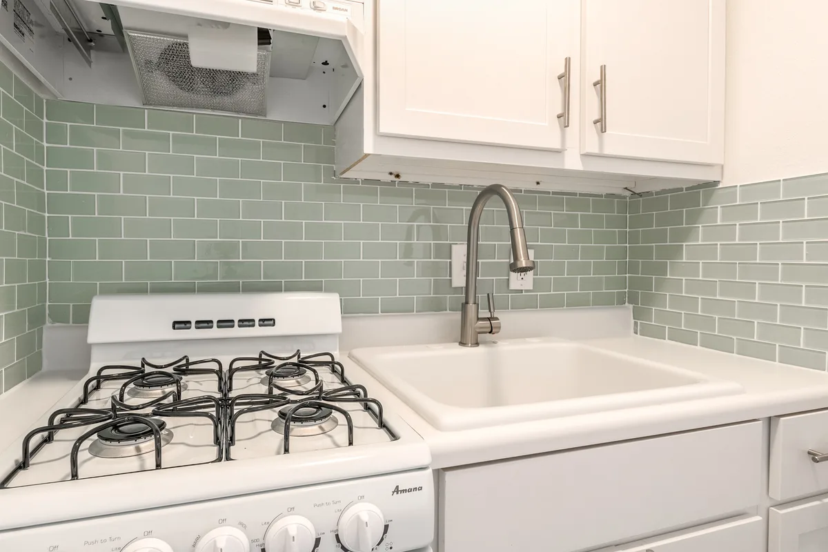 Kitchen detail with gas range, brushed-nickel faucet and glossy seafoam glass subway tile