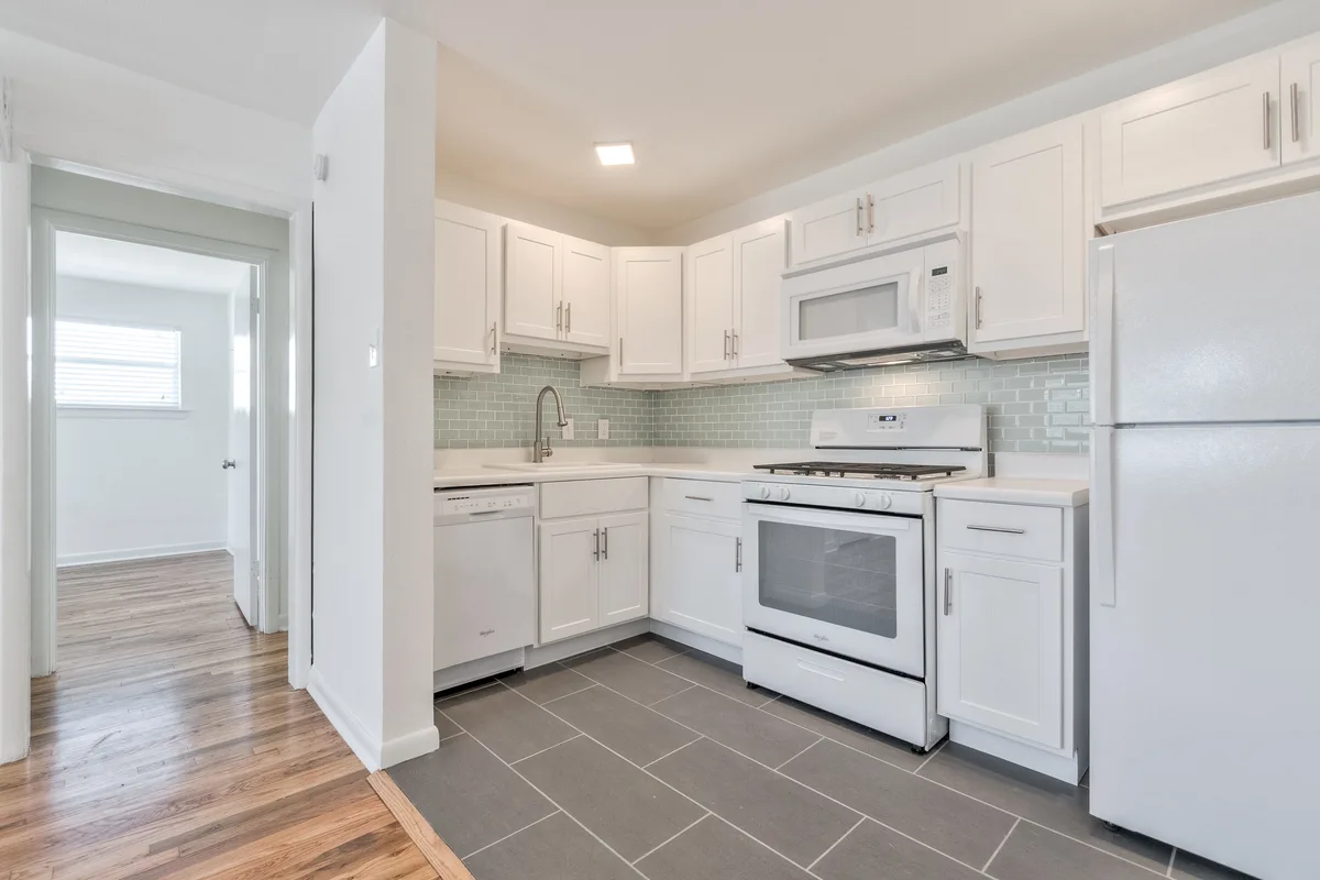 White shaker kitchen with gas range, seafoam subway-tile backsplash and gray plank tile flooring
