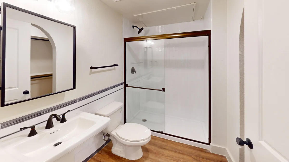 Bathroom with a black-framed mirror, wall-hung sink, bronze fixtures, and a walk-in glass shower with white tile