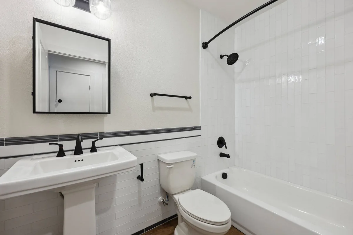 Bathroom with a black-framed mirror, pedestal sink, black fixtures, and a white-tile tub-and-shower with a curved rod