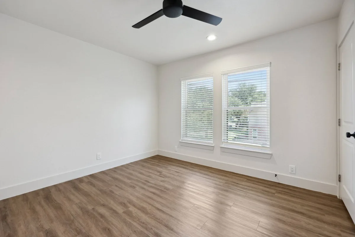 Bedroom with a black three-blade ceiling fan, corner windows with blinds, and wood-look flooring