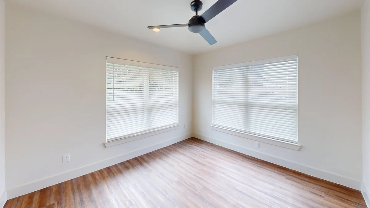 Bedroom with a dark ceiling fan and two corner windows over wood-look flooring