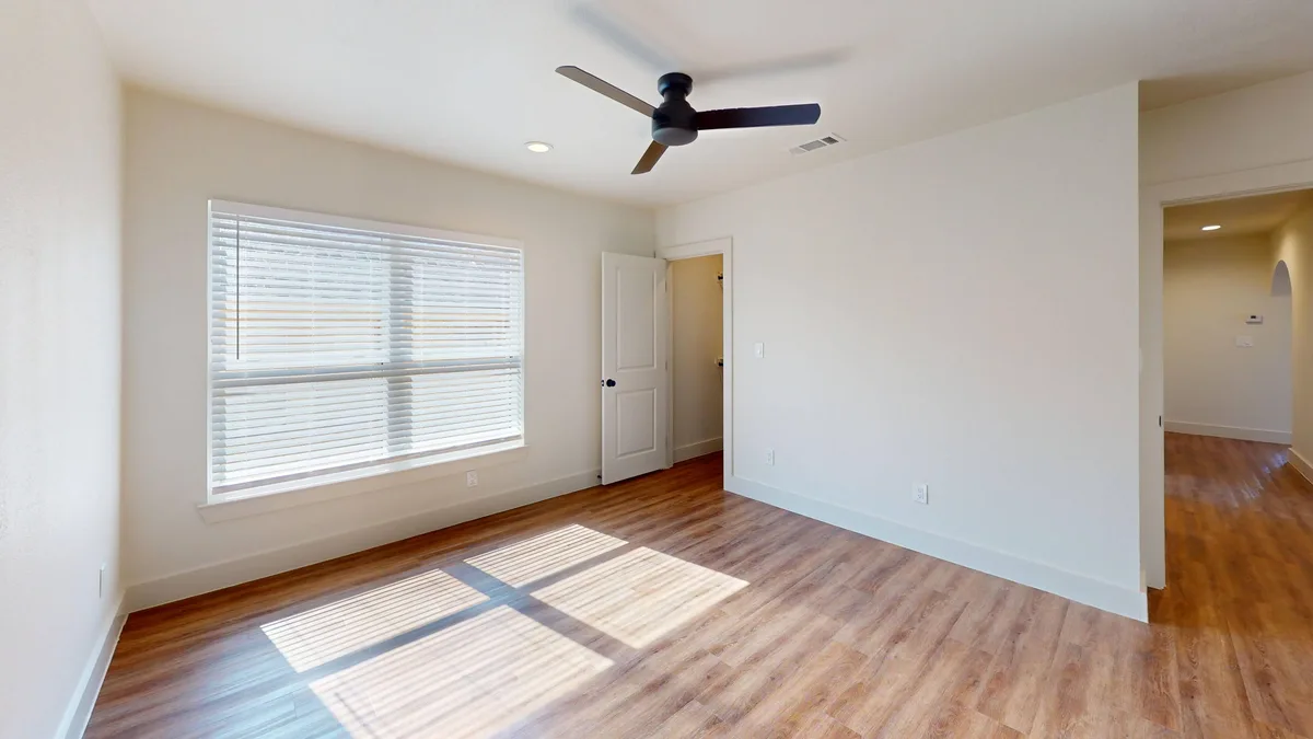 Bedroom with a black ceiling fan, a window, and a doorway opening to the hall