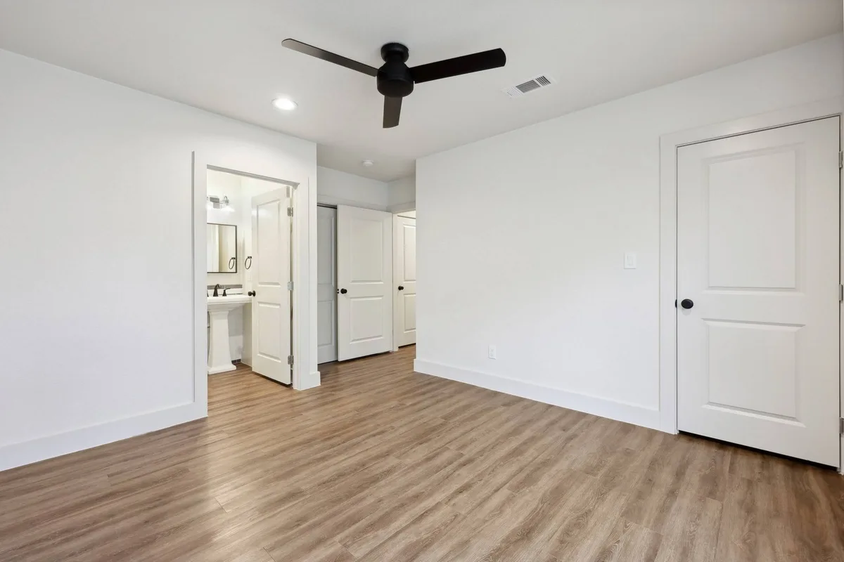 Bedroom with a black ceiling fan and an ensuite bath with a pedestal sink through the doorway