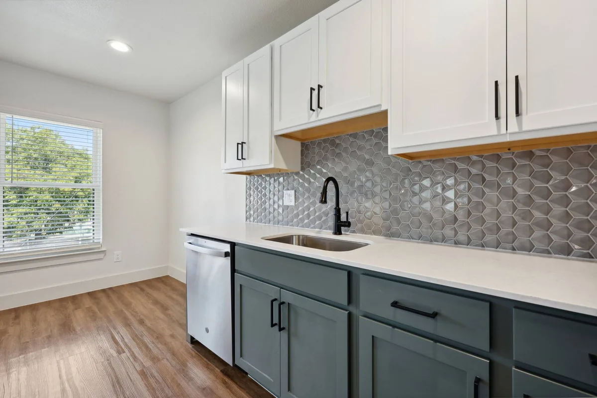 Kitchen close-up with a black gooseneck faucet, undermount sink, teal cabinets, and a silver hex-tile backsplash by a window