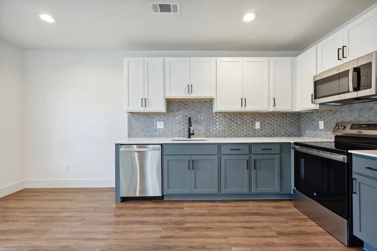 L-shaped kitchen with white uppers, blue-gray lowers, stainless appliances, and a hex-tile backsplash