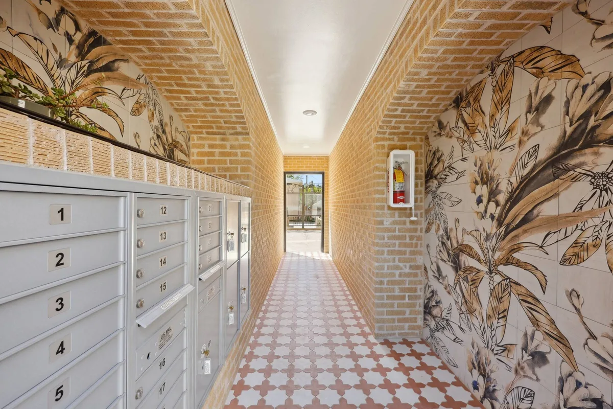 Mail room corridor with cluster mailboxes, tan brick walls, a botanical mural, and star-pattern tile floor