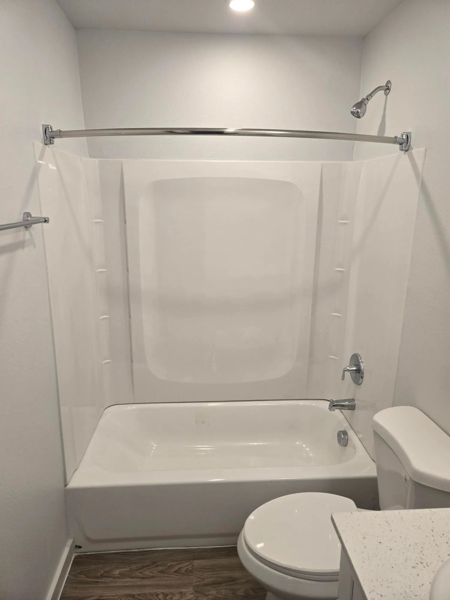 Bathroom with a white tub and shower surround, a curved curtain rod and tiled flooring